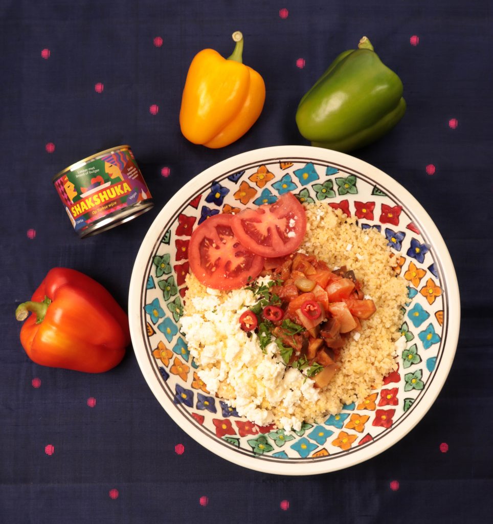 Mixblik kleine Shakshuka blik naast een bord met bulgur. Groene, gele en rode pepers op tafel.