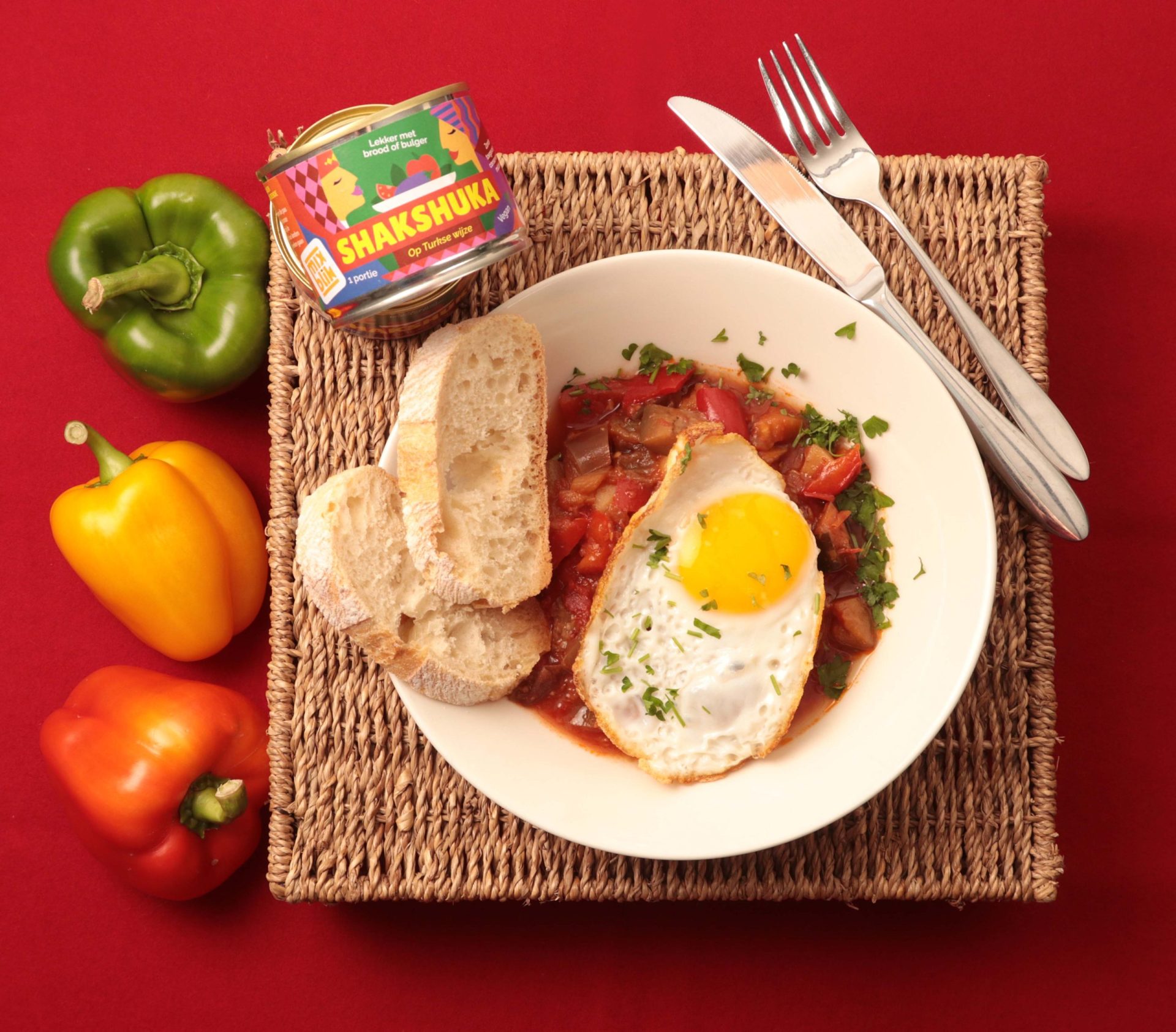 Mixblik klein shakshuka blik naast een shakshuka gerecht met ei en brood op tafel. Groene, gele en rode peper op tafel.