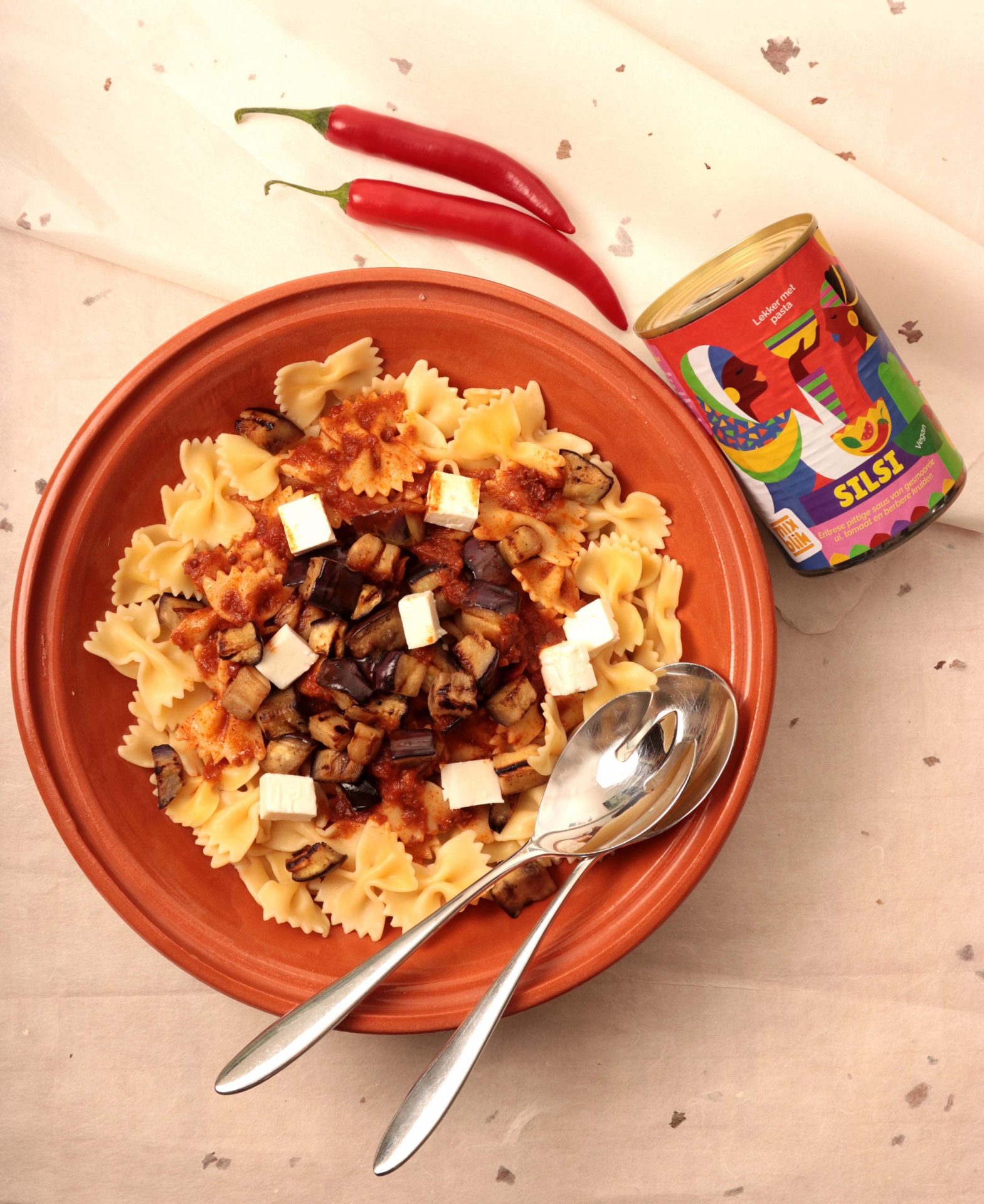 Silsi blik naast een bord met pasta. Pepers op tafel